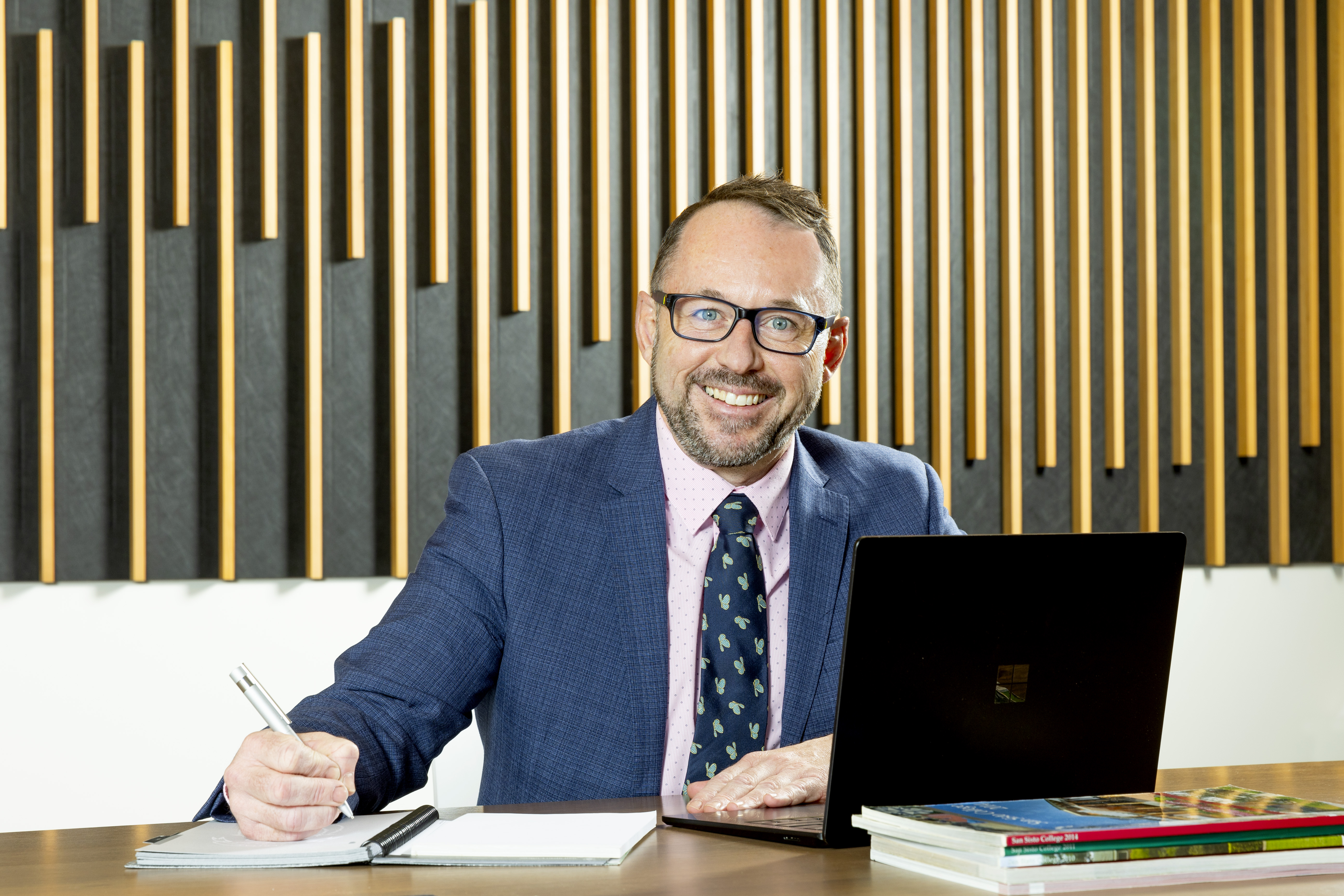 Mr Warren Bath, Principal of San Sisto College, seated with a laptop and documents, representing leadership, professionalism and connection with the school community