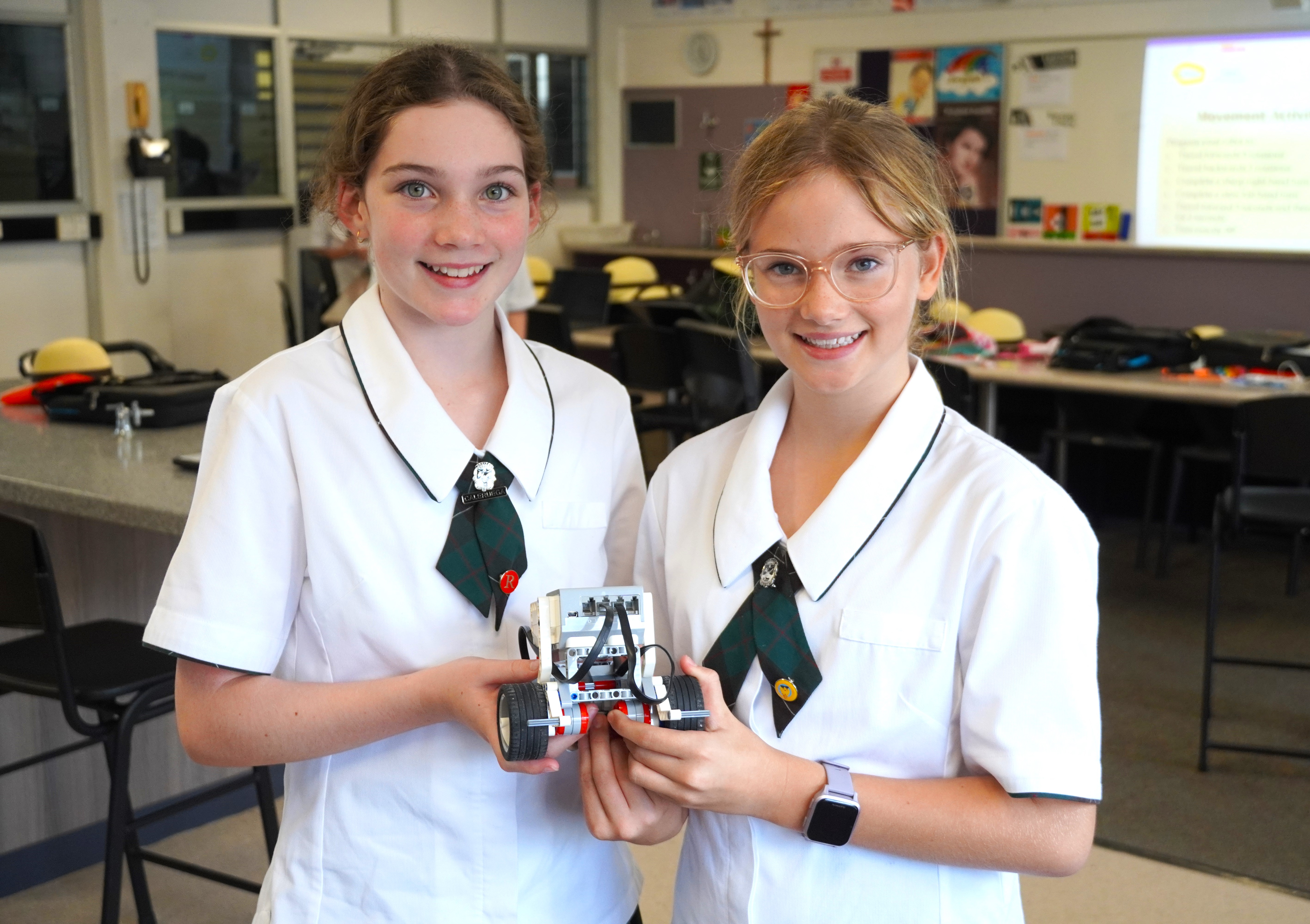 Students standing together in a classroom holding a robotics project, highlighting collaboration innovation and hands on STEM learning at San Sisto College